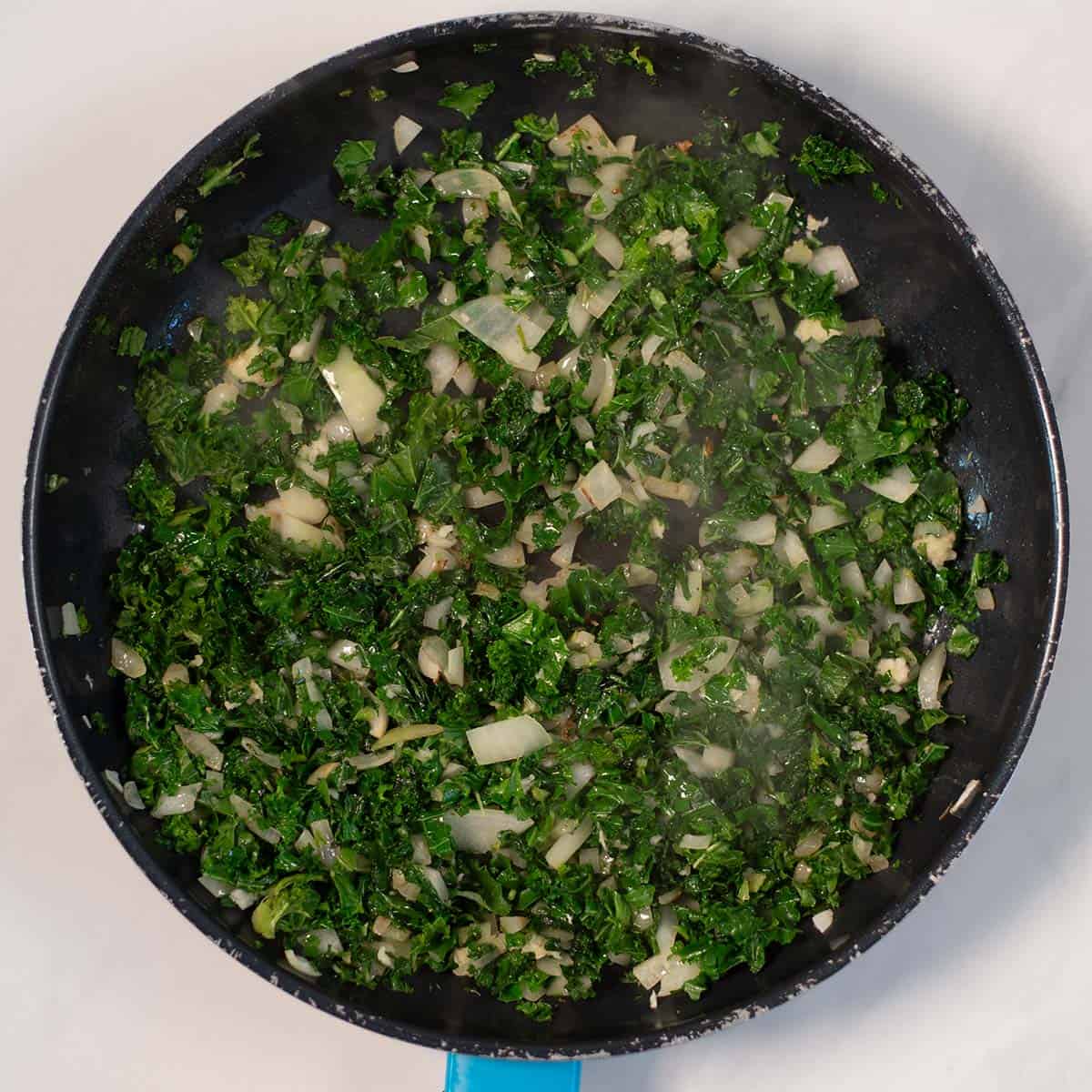 Onions and kale a fried in a pan.