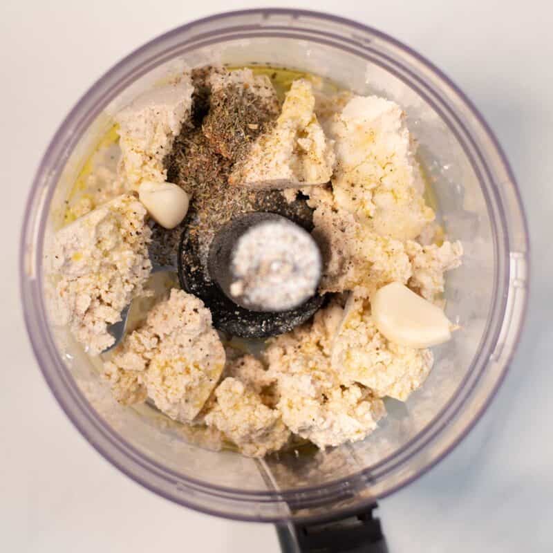 Ingredients for the tofy ricotta are given to the bowl of a food processor.