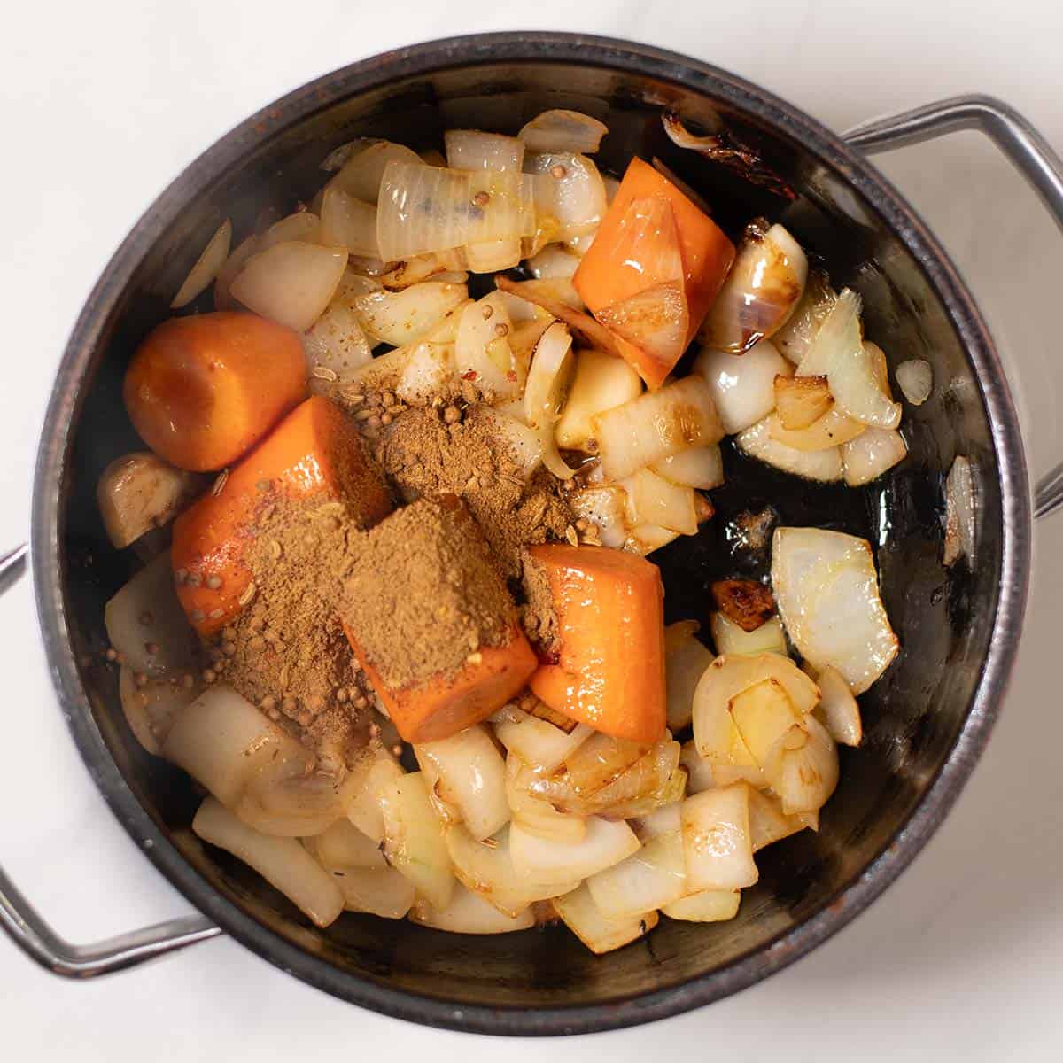 Onions and carrots are fried in a pot.