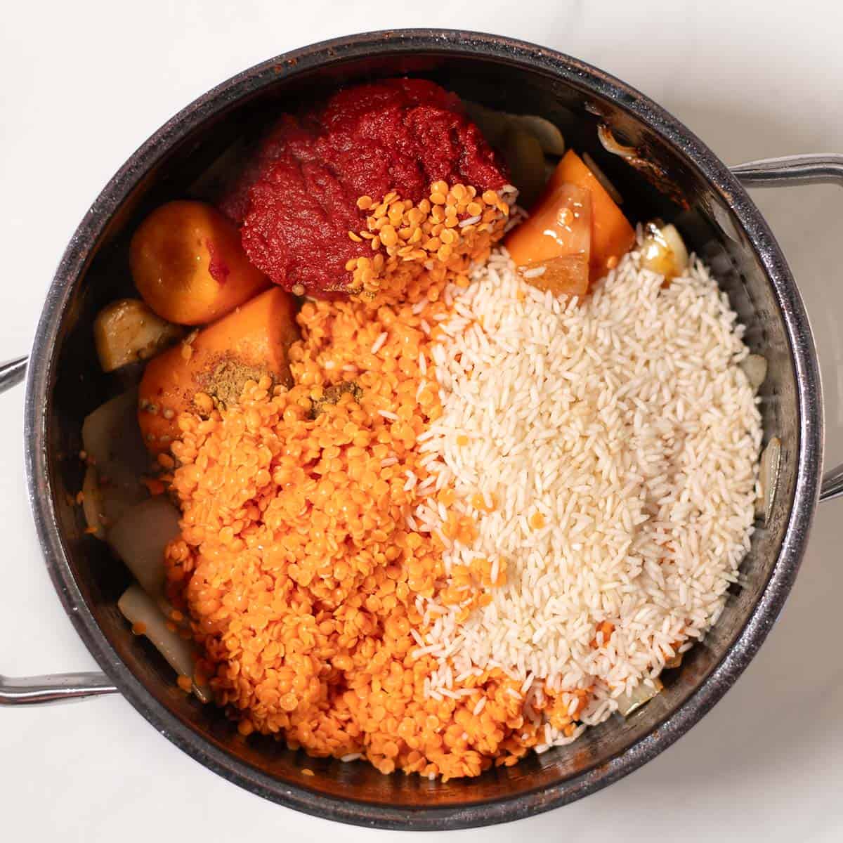 Tomato paste, red lentils and white rice are given to the pot.