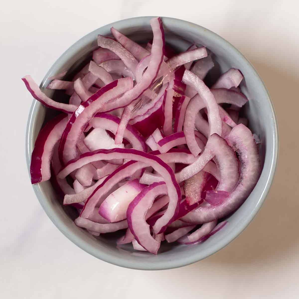Red onion slices marinate and soften in vinegar.