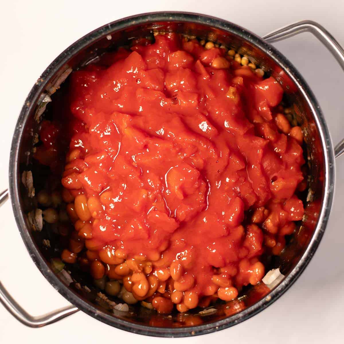 Beans, tomatoes and broth are added to the pot with vegetables.