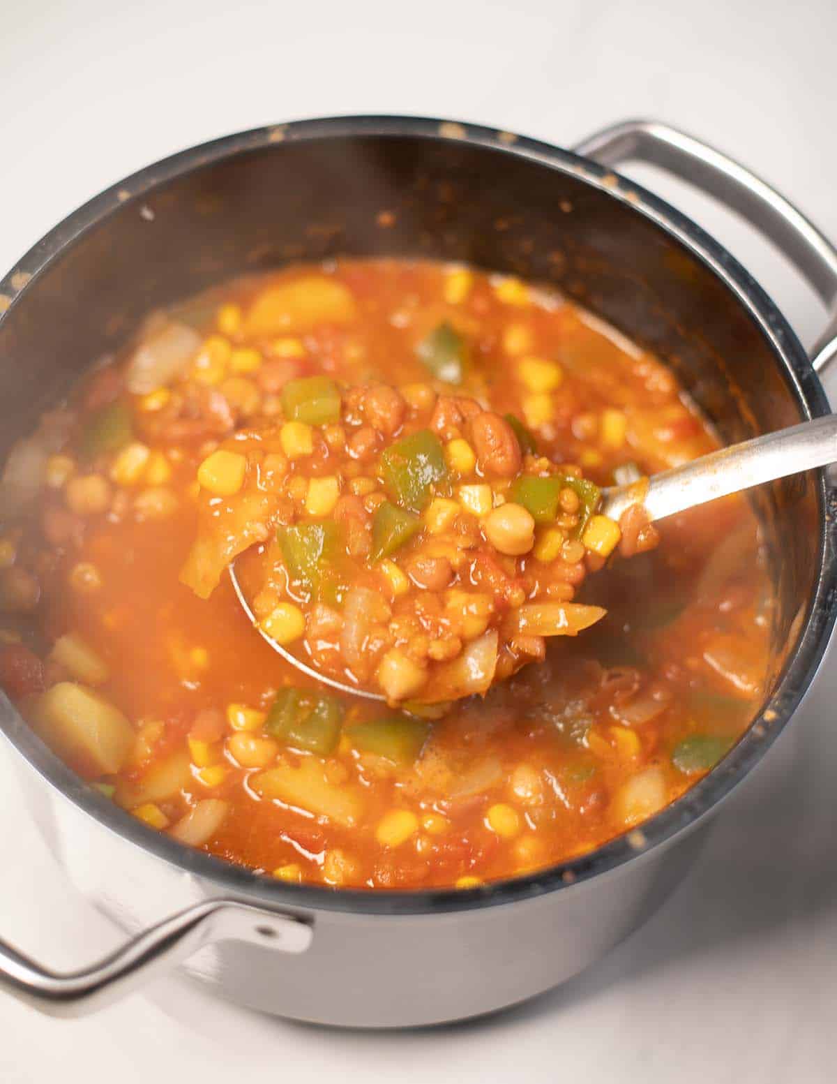 A large spoon of Vegan Cowboy Soup is lifted from the pot.