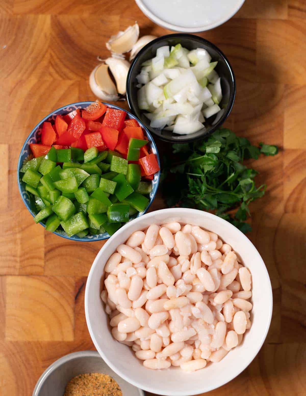 Bowl of white beans with chopped green bell peppers and onions on a wooden counter.