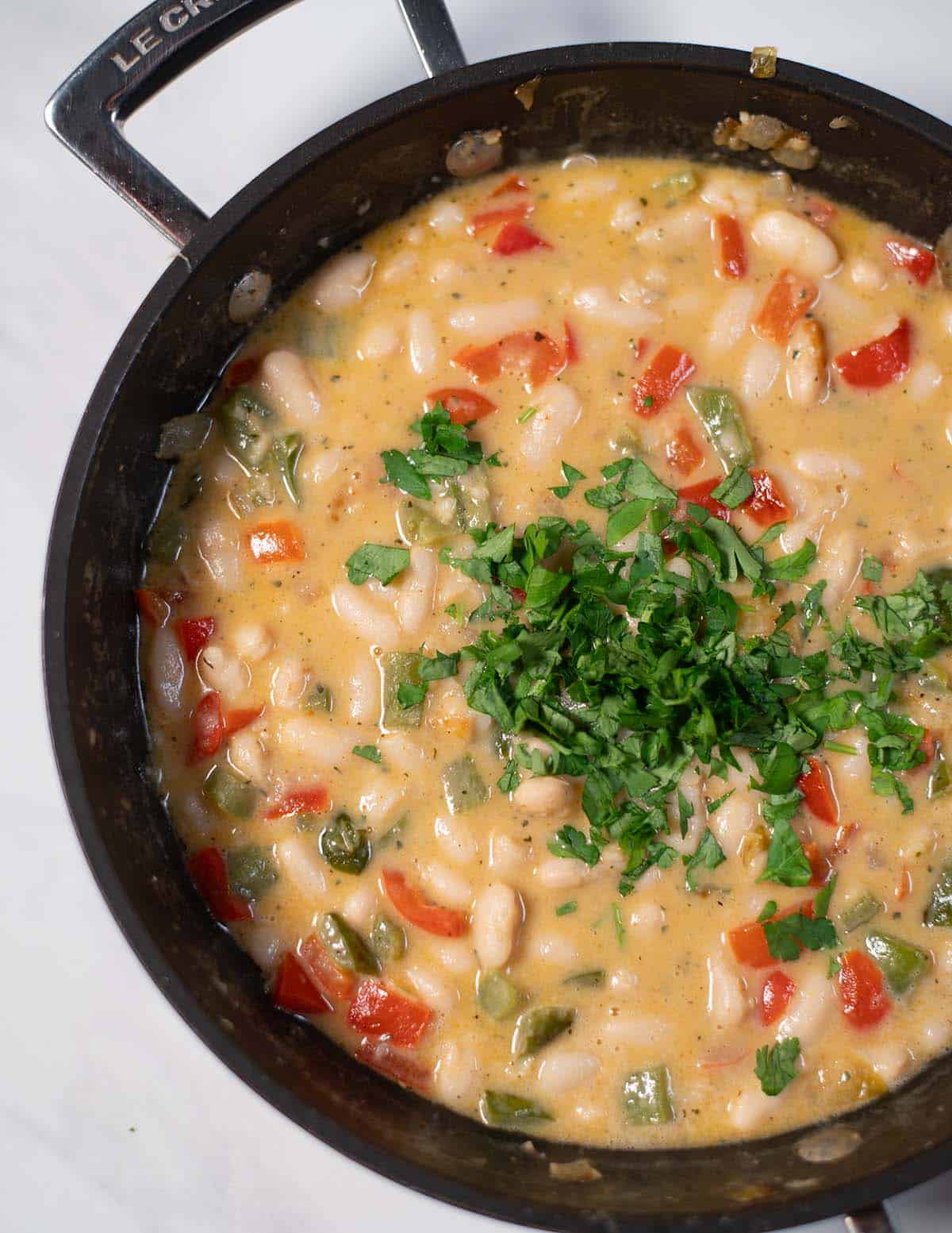 Creamy Cajun white beans in a skillet topped with chopped parsley.