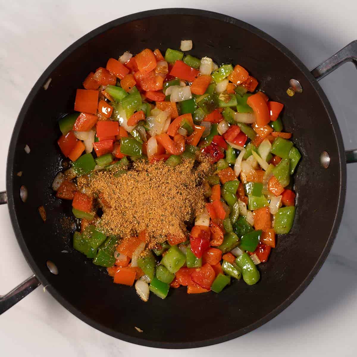Colorful sautéed peppers and onions in pan with spices.