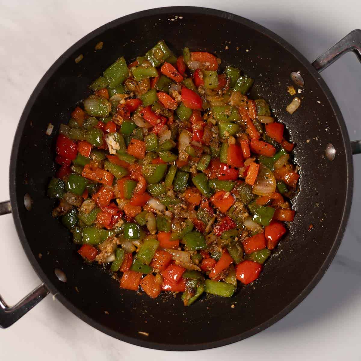 Diced red and green bell peppers sautéed in a skillet.