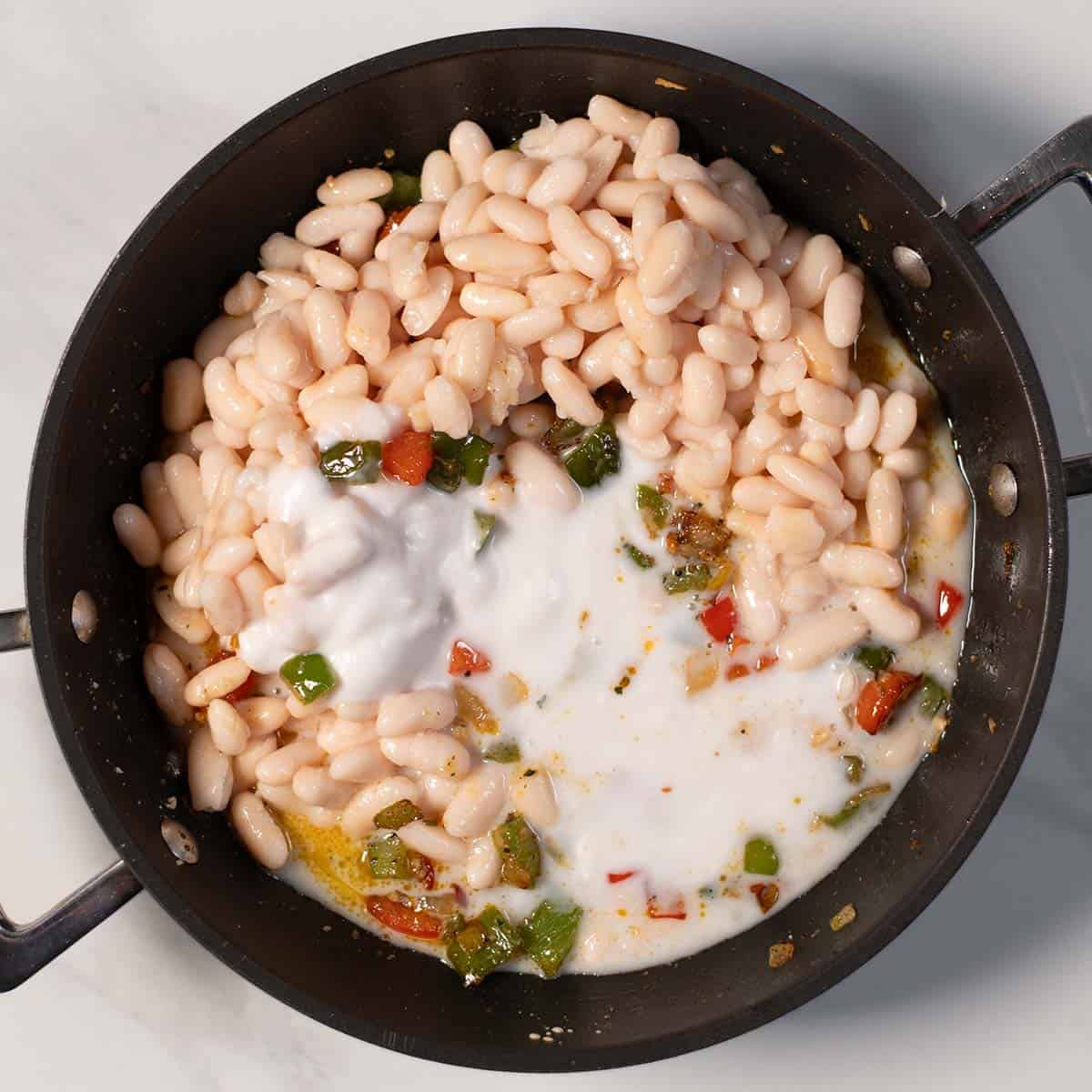 Creamy Cajun white beans in a skillet with peppers and herbs.
