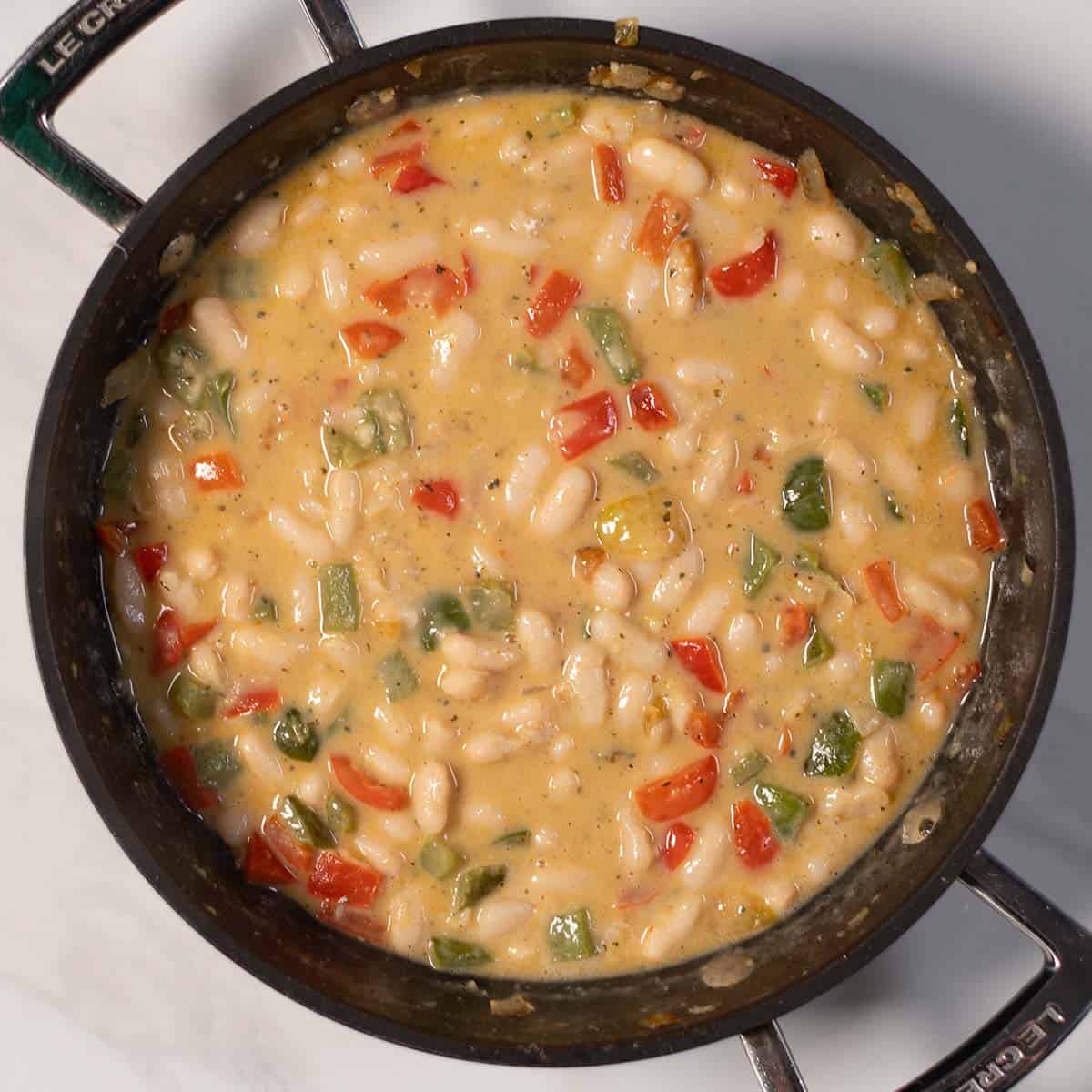 Creamy white bean dish in a skillet with bell peppers and onions.