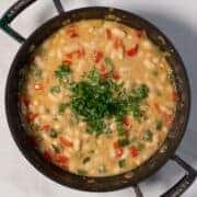 Creamy Cajun white beans in a skillet with chopped herbs.