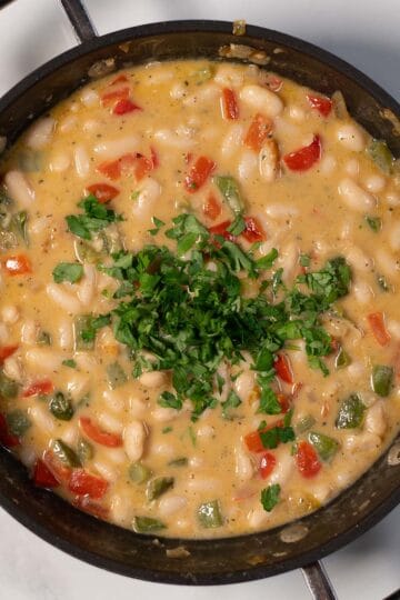 Creamy Cajun white beans in a skillet with chopped herbs.