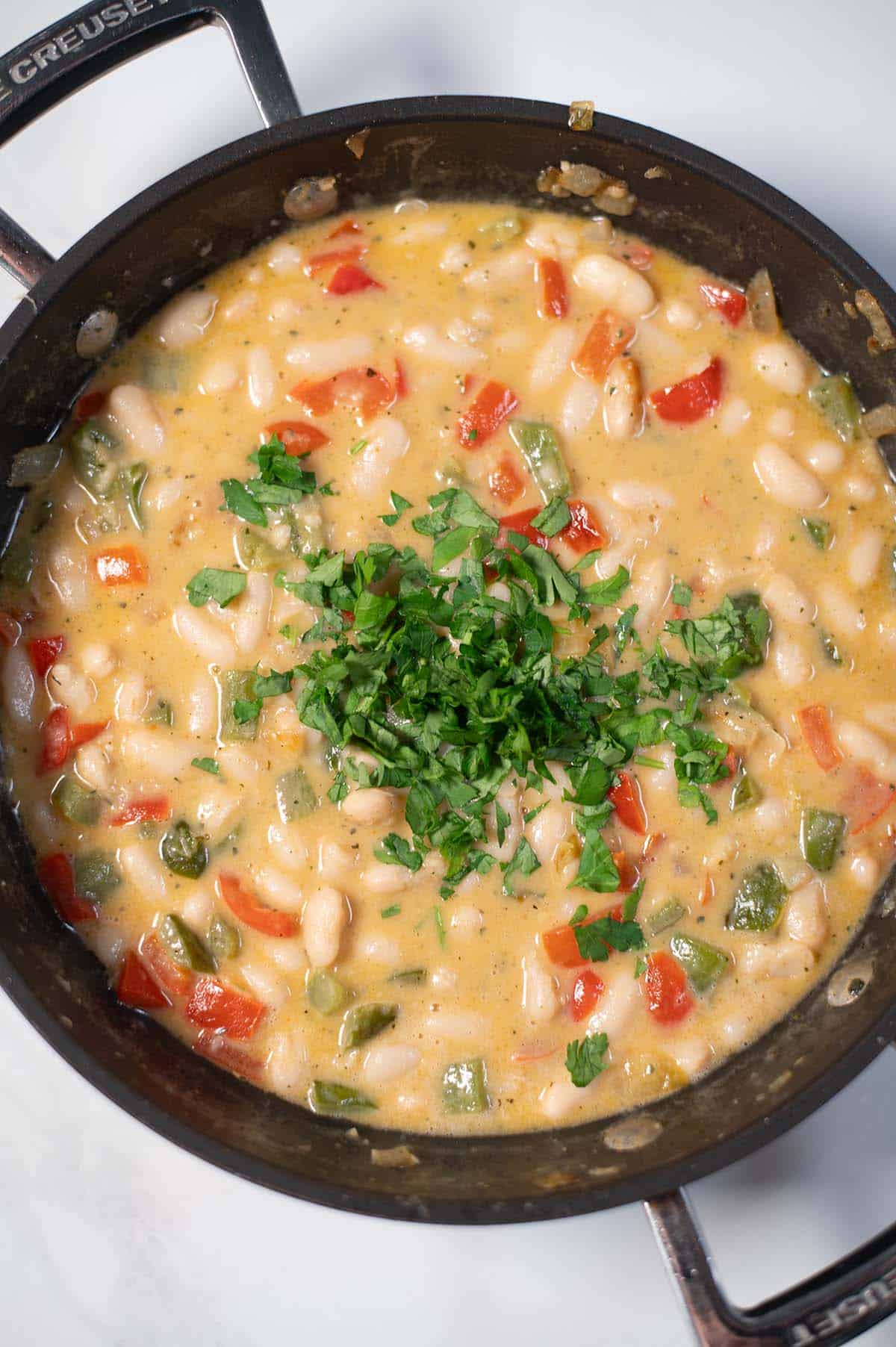 Creamy Cajun white beans with peppers and parsley in a skillet.