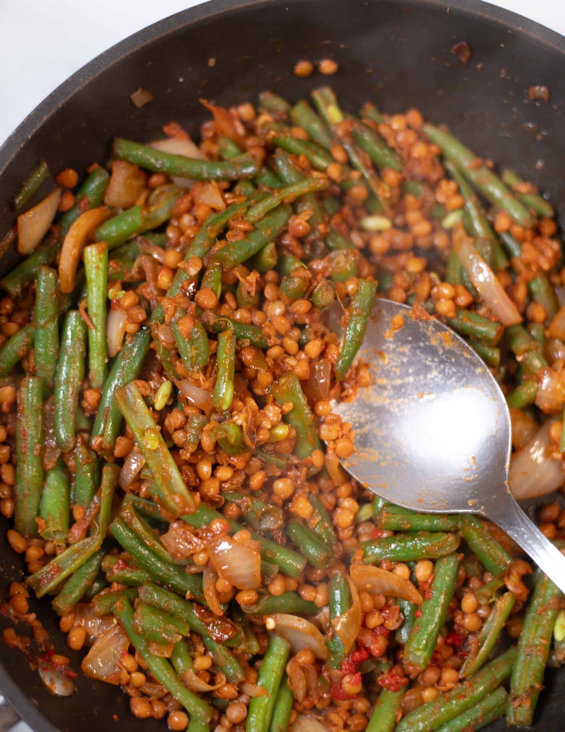 Stir-fried green beans with lentils and onions in a skillet.