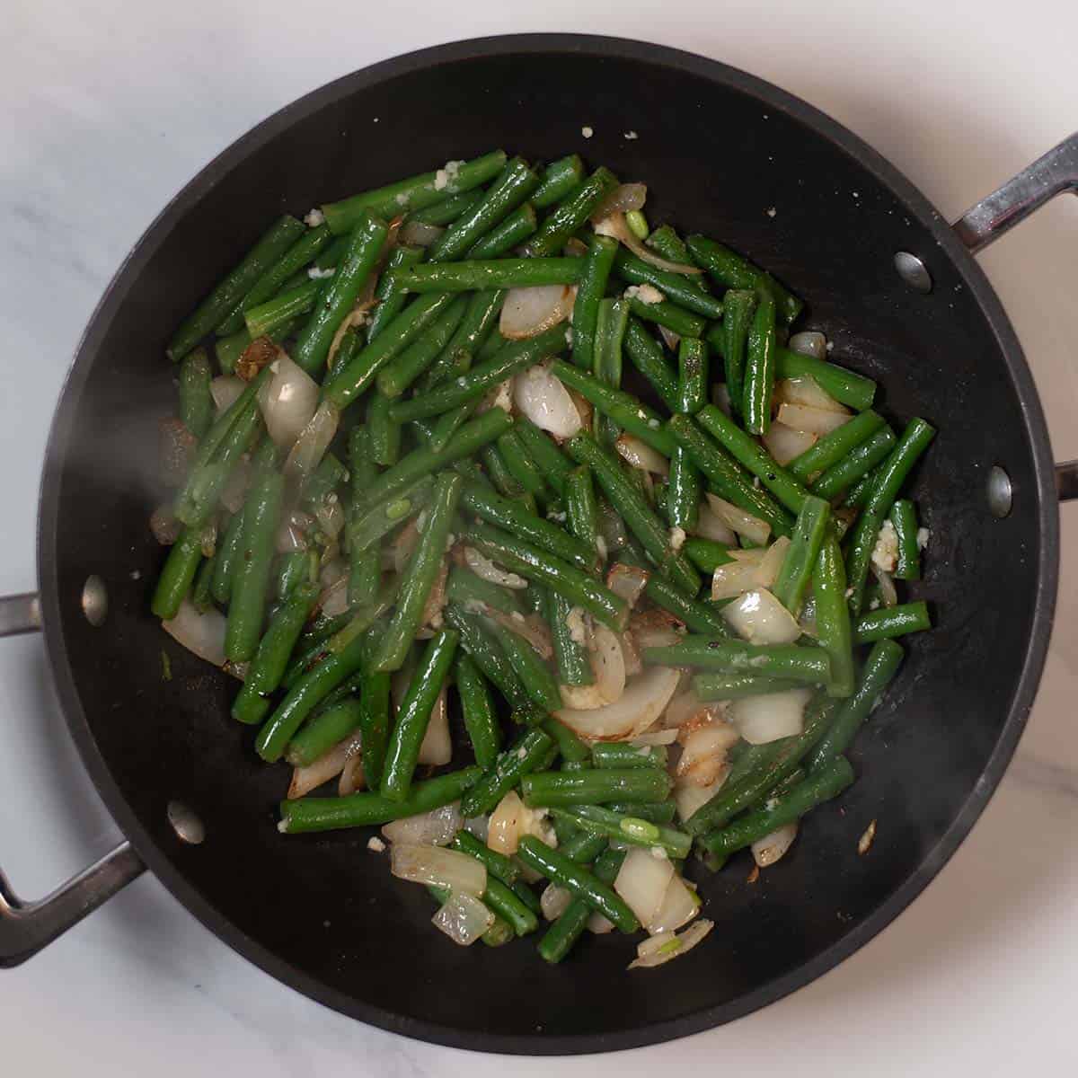 Green beans and onions cooking in a skillet for healthy side dish.