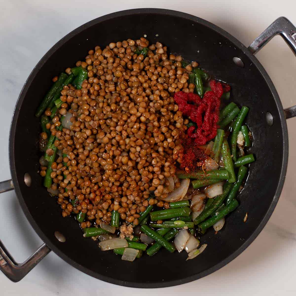 Green beans, lentils, onions, and spices in a skillet for healthy meal.
