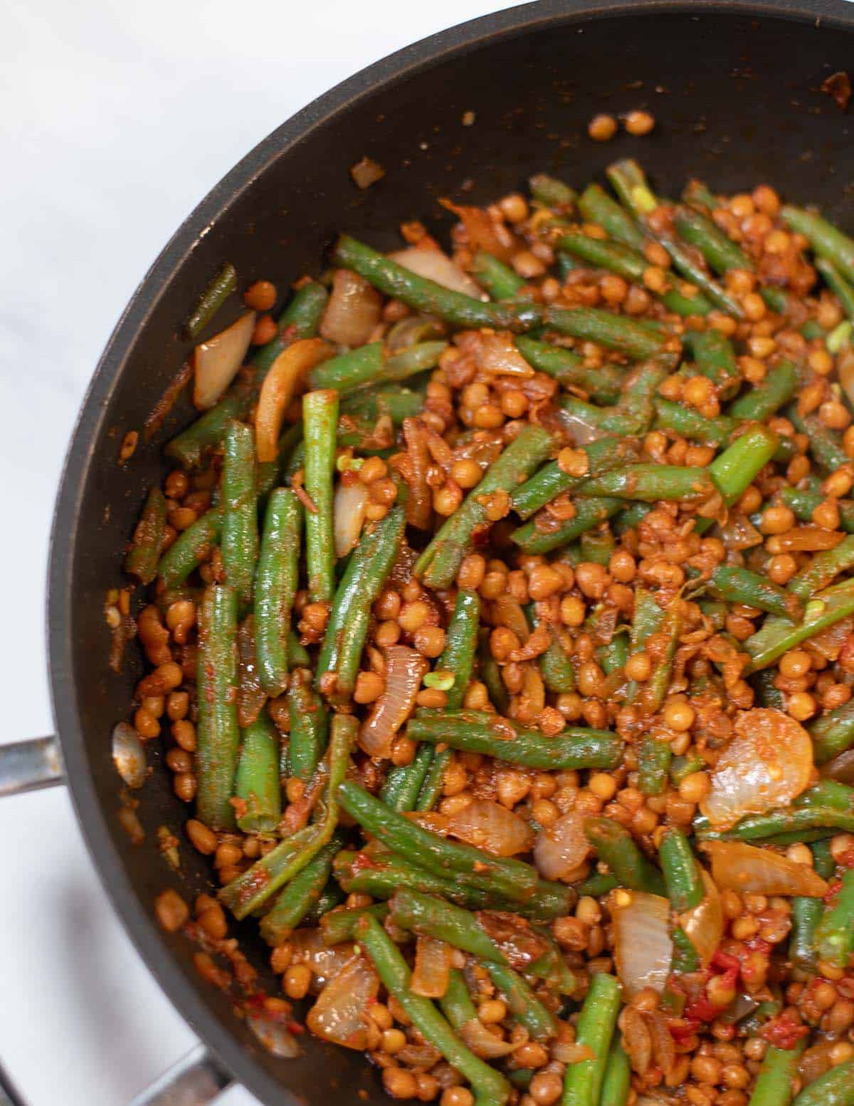 Green beans and lentils cooked with spices in a skillet for a healthy meal.