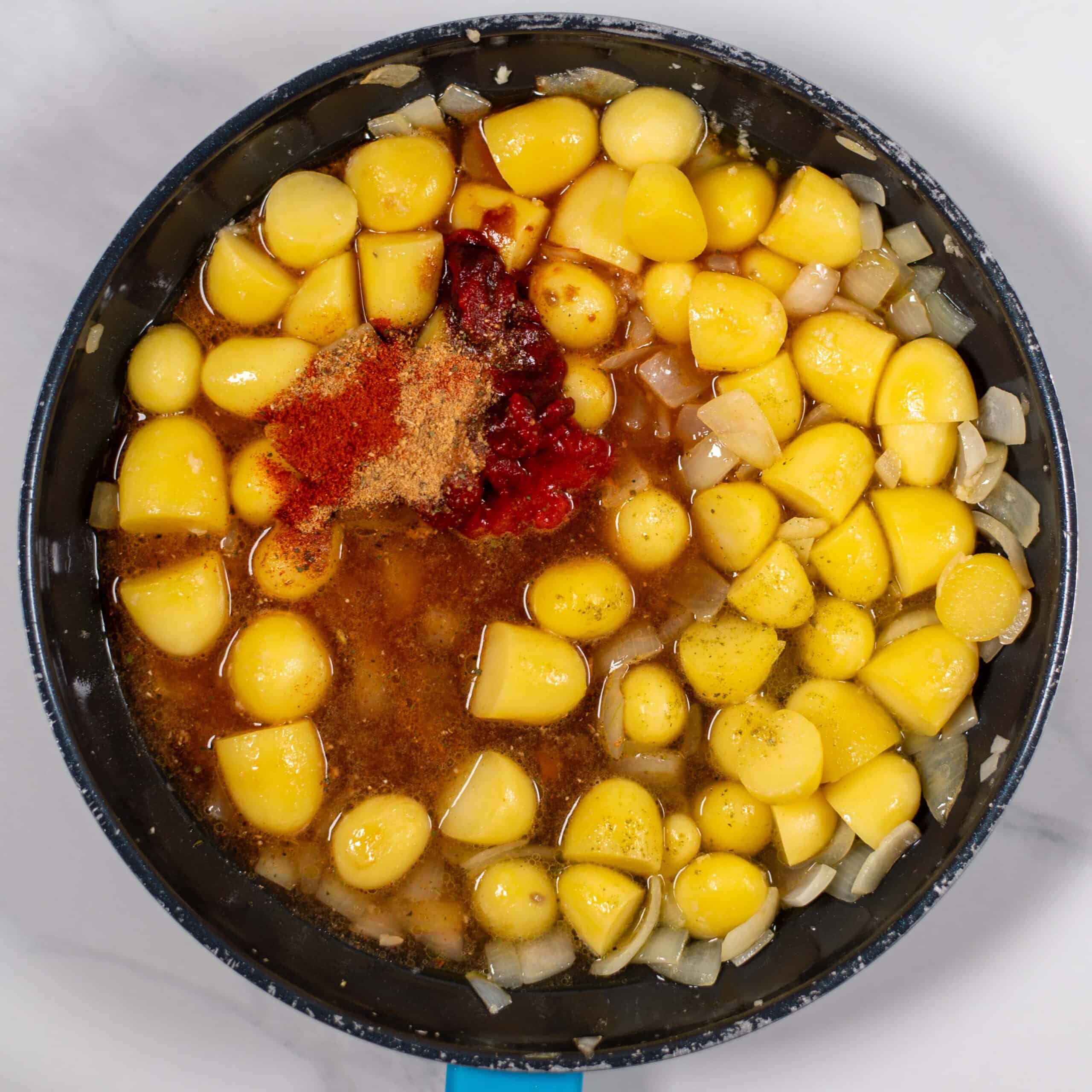 Uncooked yellow potatoes with spices and onions in a skillet.