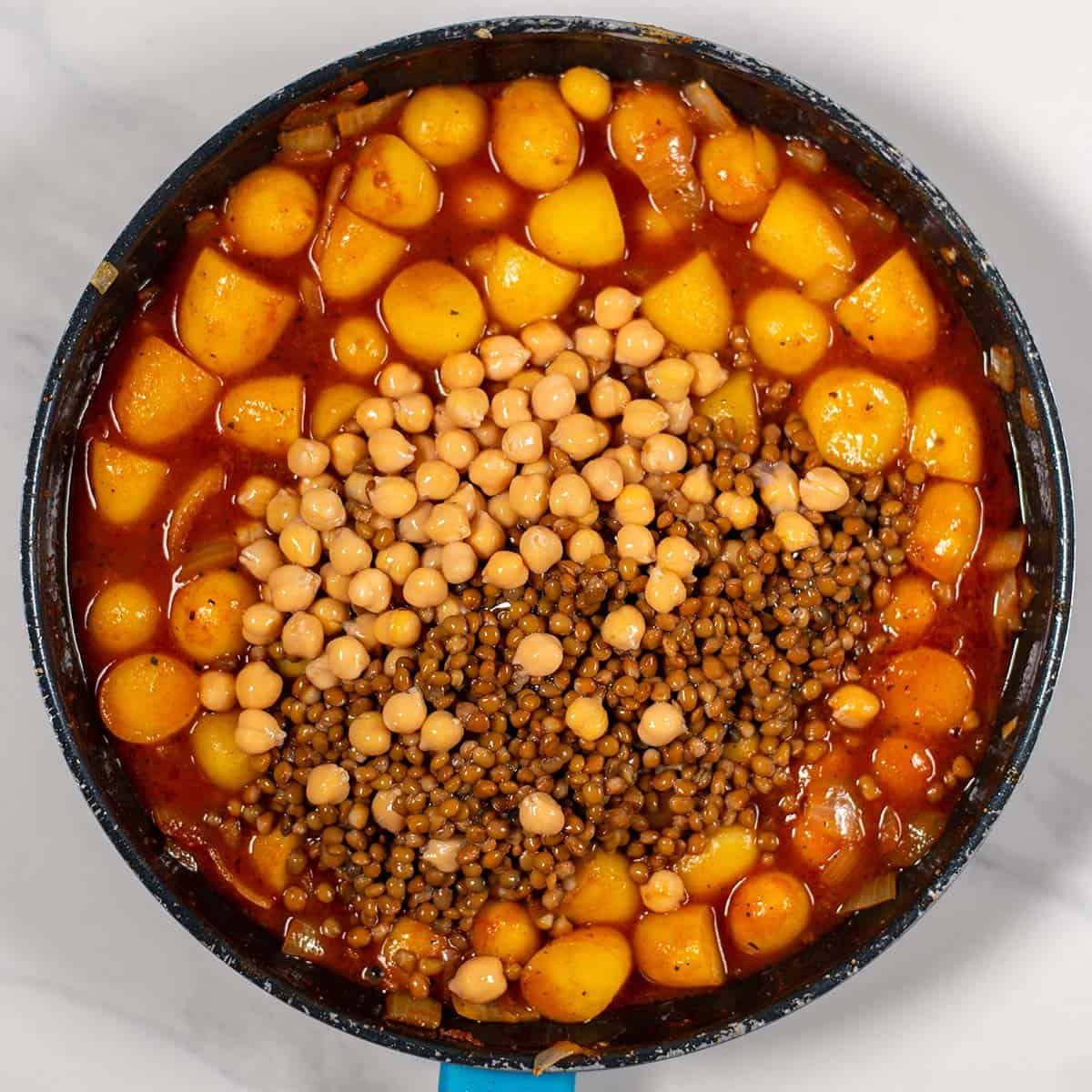 Potatoes and lentils cooking in a flavorful broth in a black pot.