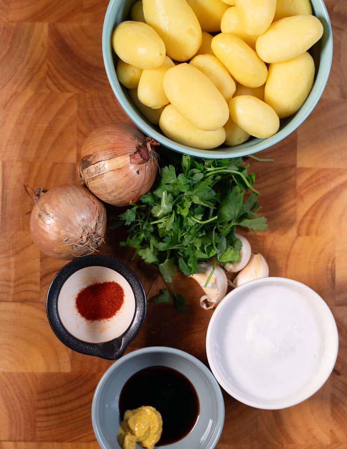 Creamy French onion potatoes with onions, herbs, and bowls of condiments on a wooden surface.