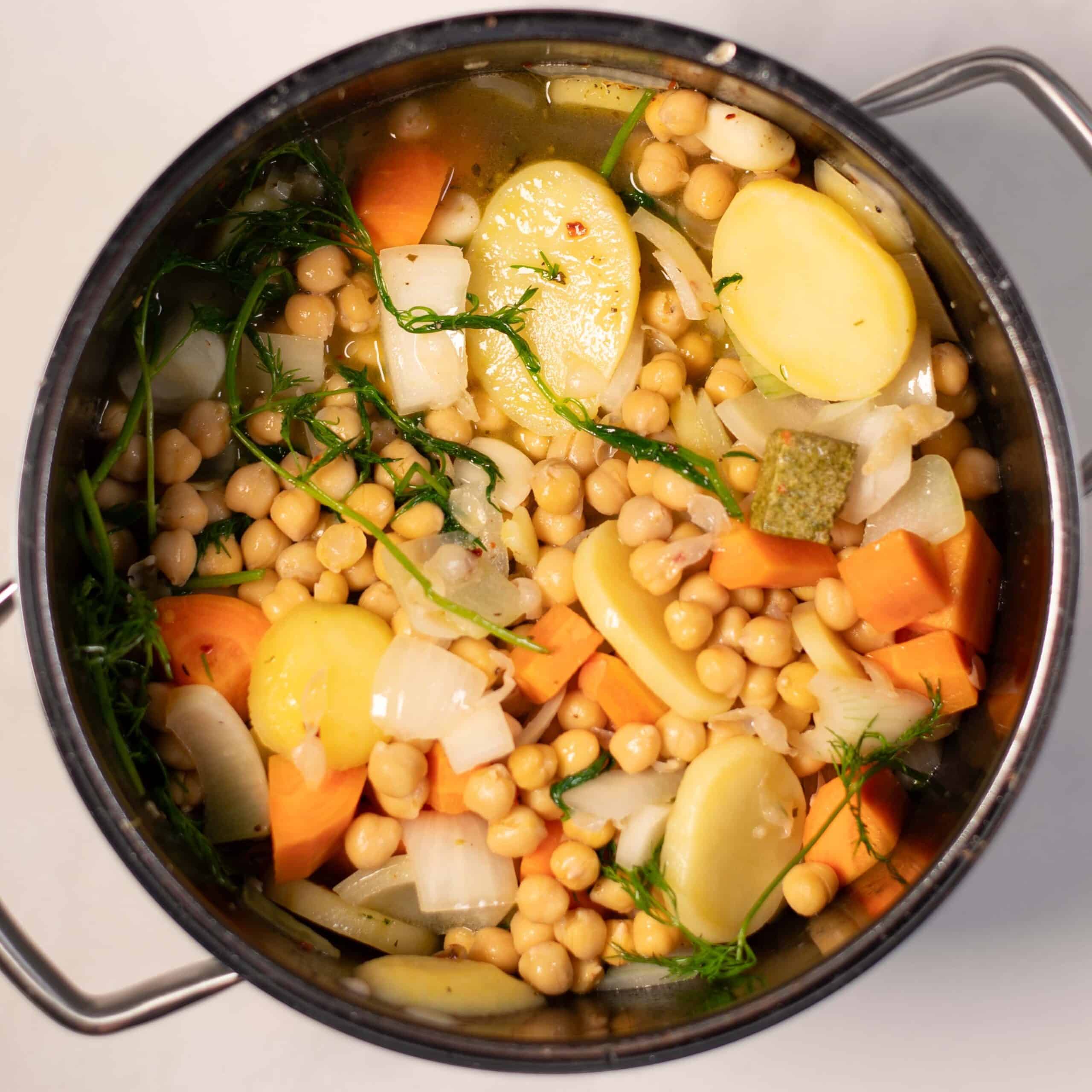 Close-up of chickpeas, vegetables, and herbs in a pot for Greek soup.