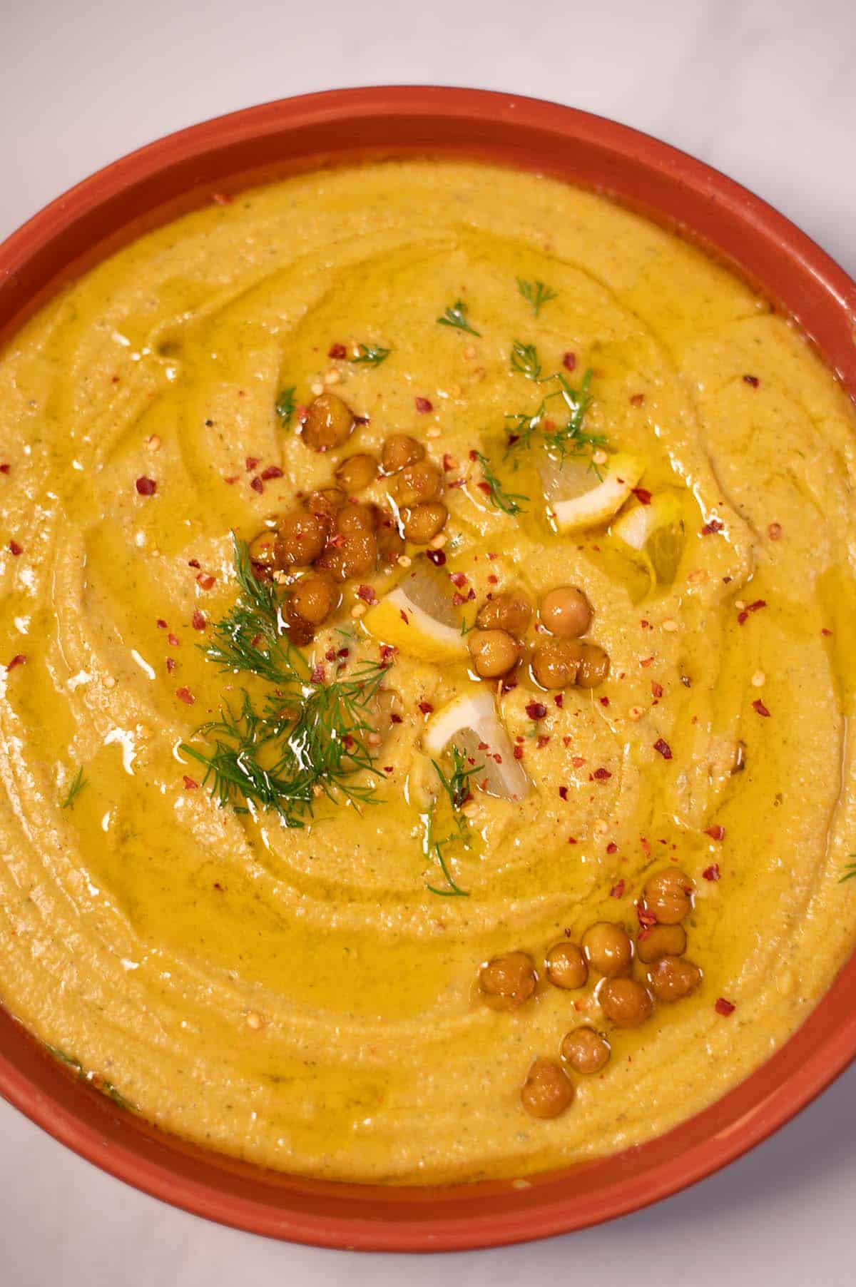 Creamy Greek chickpea soup garnished with herbs and spices in a terracotta bowl.