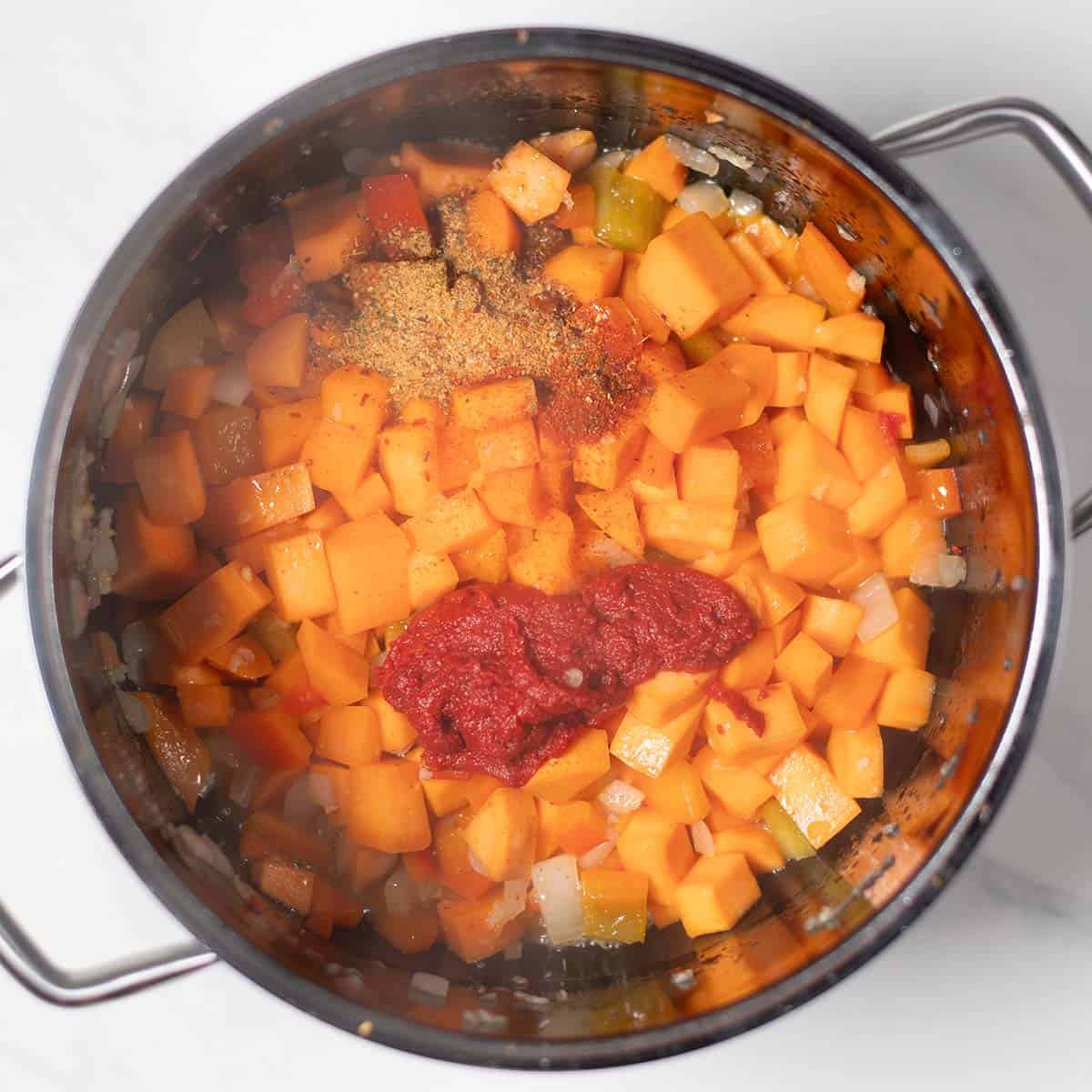 Diced sweet potatoes, onions, and tomato paste in a pot for chili.