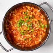 Hearty sweet potato chili with white beans and green onions in a pot.