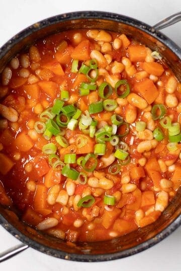 Hearty sweet potato chili with white beans and green onions in a pot.
