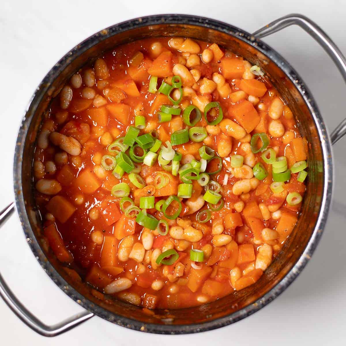 Hearty sweet potato chili with white beans and green onions in a pot.