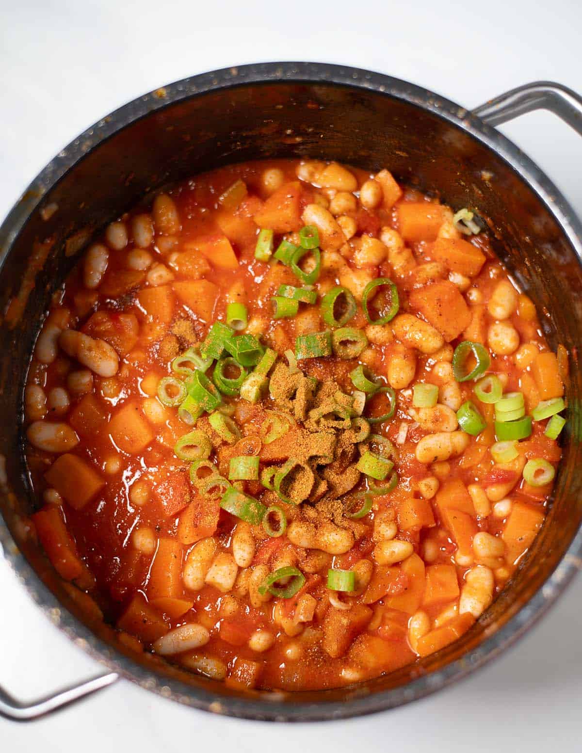 Hearty sweet potato chili with white beans and green onions in a pot.