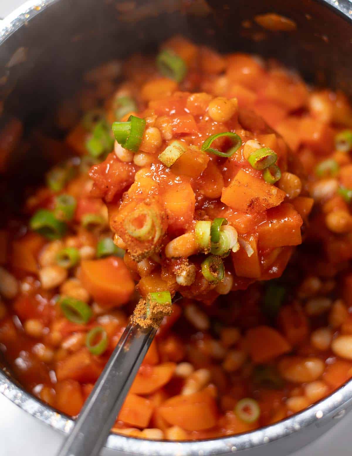Close-up of sweet potato chili with white beans and green onions in a pot.