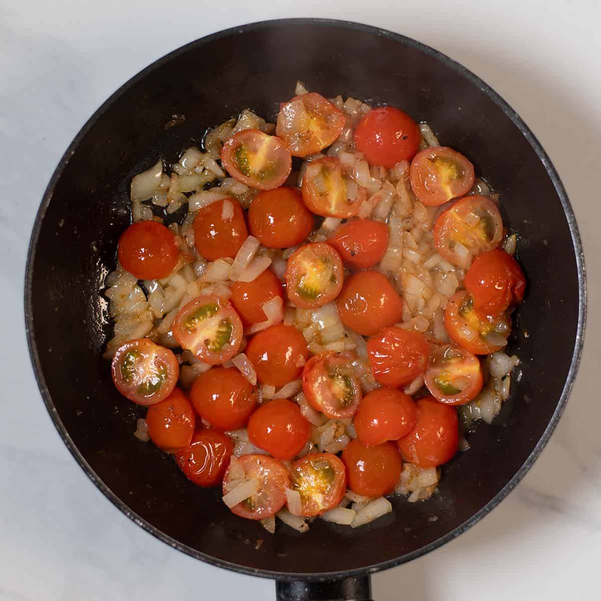 Cherry tomatoes and chopped onions cooking in a skillet for a recipe.