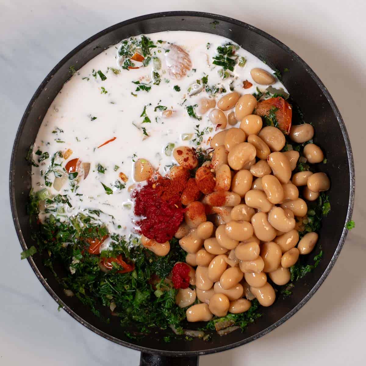 Creamy Tuscan kale and white beans in a skillet with herbs and spices.