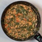Creamy kale and white beans in a skillet with tomatoes and herbs.