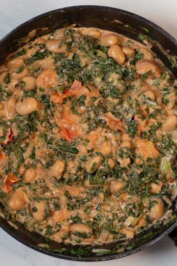 Creamy kale and white beans in a skillet with tomatoes and herbs.