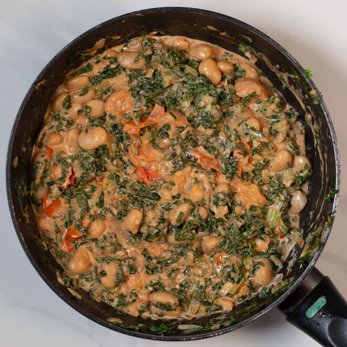 Creamy kale and white beans in a skillet with tomatoes and herbs.