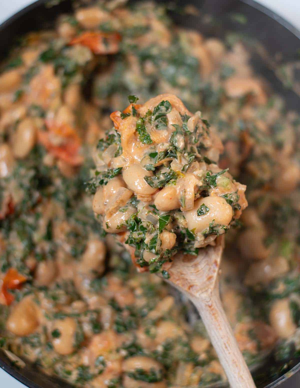 Creamy Tuscan kale and white beans in a skillet with a spoonful served.